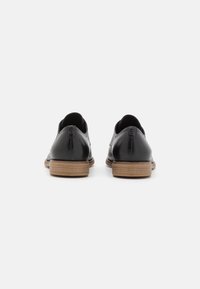Chaussures en cuir noir à finition lisse, profil bas, et talon empilé marron clair. Présentent des détails minimalistes et des bords arrondis.