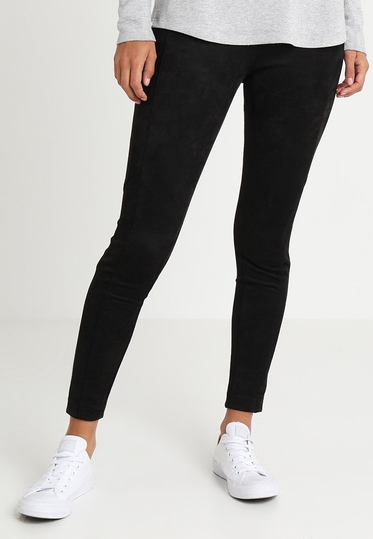 Leggings noirs extensibles avec une finition douce et texturée, ayant une coupe ajustée. Associés à des baskets blanches pour le contraste.