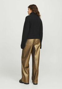 Maglione nero a collo alto lavorato a maglia abbinato a pantaloni larghi dorati lucidi, con una superficie texturizzata e colori a contrasto.