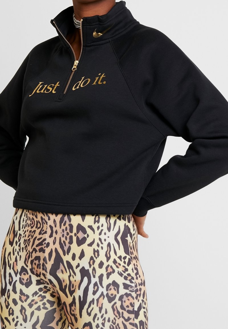 Person wearing a black cropped sweatshirt with gold "Just do it." text and gold Nike swoosh, paired with leopard print leggings.