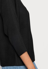 Maglione nero lavorato a maglia con trama a coste, maniche a tre quarti e vestibilità morbida, abbinato a jeans di denim azzurro chiaro.