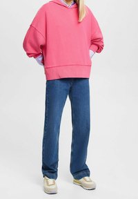 Rosa stor hoodie med huva, kombinerad med lösa blå denimjeans och beige sneakers med lila detaljer. Enkelt mönster och mjuk textur.