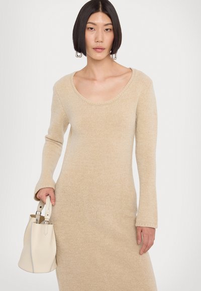 Abito lavorato a maglia beige con maniche lunghe e scollatura a girocollo. Tessuto liscio; abbinato a una piccola borsa crema tenuta in una mano.