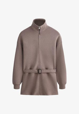 Jachetă taupe cu mâneci lungi, guler înalt, fermoar frontal, curea reglabilă cu cataramă și manșete strânse pe fundal alb.