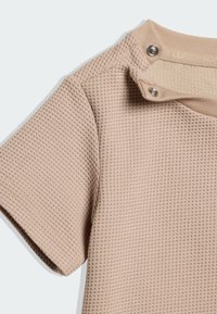 Camiseta beige de manga corta con tejido de gofre, cuello acanalado y dos botones de presión plateados en el hombro.