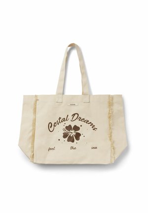 Sac fourre-tout en toile beige avec doubles poignées, bords verticaux effilochés, et texte marron « Costal Dreams feel the sea » entourant un motif de fleur d’hibiscus.
