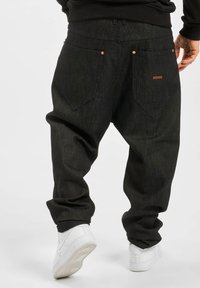 Black denim pants with a relaxed fit, featuring double back pockets, copper hardware, and a small brown tag on the right pocket.