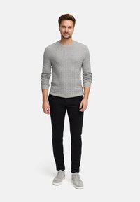 Grå strikkegenser med et teksturert mønster, kombinert med sorte slim-fit bukser og lysegrå sneakers, stående mot en hvit bakgrunn.