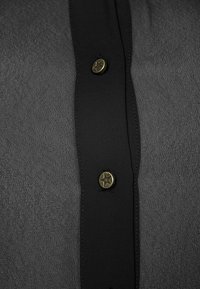Camicia nera a maniche lunghe con tessuto grigio testurizzato. Presenta bottoni metallici a forma di stella lungo la patta e un tessuto liscio a contrasto nel colletto.