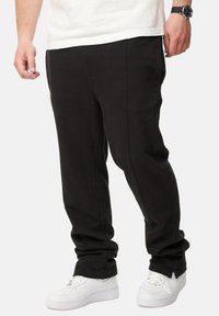 Schwarze Sweatpants mit lockerer Passform, mit Seitennähten und Bündchen. Kombiniert mit weißen Sneakern für einen Kontrast. Weicher Stoff fühlbar.