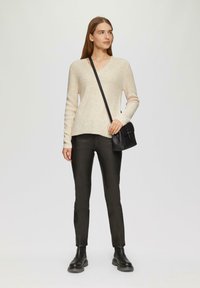 Jasny sweter z dekoltem w serek o rypsowym splocie, w połączeniu z czarnymi spodniami o dopasowanym kroju i czarną torebką typu crossbody. Stylizację dopełniają czarne botki za kostkę.