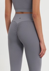 Leggings de sport gri, cu un model texturat în formă de fagure și talie înaltă, concepute pentru suport și flexibilitate în timpul antrenamentelor.