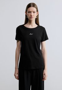 Črna bombažna majica s kratkimi rokavi in okroglim izrezom, na prsih ima belo izvezen napis, preprost dizajn z ohlapnim krojem.