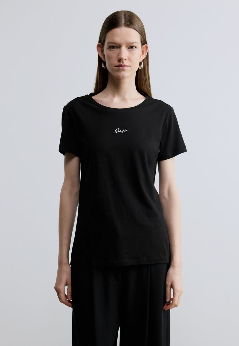 Črna bombažna majica s kratkimi rokavi in okroglim izrezom, na prsih ima belo izvezen napis, preprost dizajn z ohlapnim krojem.