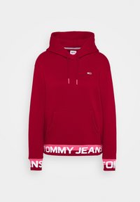 Sudadera roja con bolsillos frontales, capucha con cordón y logo "TOMMY JEANS" en rosa en el dobladillo. Fabricada en un tejido suave y texturado.