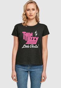 Must rõngas must puuvillane T-särk, millel on roosa ja valge graafiline trükk, mis �ütleb "Thin Lizzy Little Darlin'" koos välgu aktsentidega.