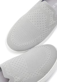 Helle graue Slipper aus strukturiertem Strickmaterial mit einem belüfteten Design, einer weißen Gummisohle und nahtloser Konstruktion.