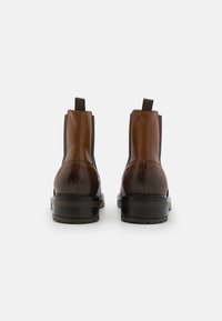 Brune lær ankle støvler med elastiske sidepaneler, bageste trækkebånd og en tekstureret sort gummisål. Glat finish med rundet tådesign.