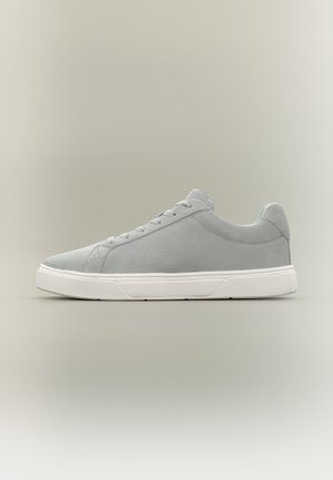 Lichtgrijze lage sneaker met witte rubberen zool en bijpassende grijze veters, zijaanzicht op een neutrale achtergrond.