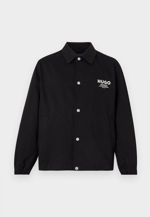 Schwarze Jacke mit Knöpfen und Kragen, elastischen Bündchen, seitlichen Taschen und weißem "HUGO"-Logo auf der linken Brust.