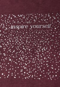 Bordová tkanina s textem "inspiruj se" v bílé barvě, obklopená stříbrnými tečkami, vytvářejícími texturovaný vzhled.