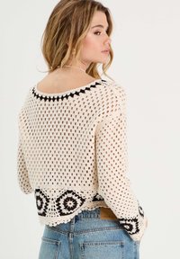 Jersey de ganchillo en crema con acentos geométricos en negro en el dobladillo. Presenta un cuello redondo y una trama abierta para una textura ligera.