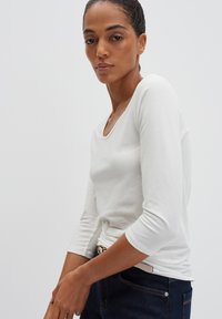 Weißes Langarmshirt mit einem runden Ausschnitt, schmaler Passform, glatter Textur und Dreiviertelärmeln, kombiniert mit dunklen Jeans.