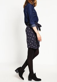 Camisa de denim de manga larga, combinada con una falda azul marino con un patrón delicado. La modelo lleva medias negras opacas y botines.