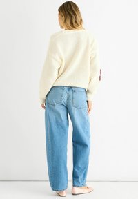 Cream-colored knitted sweater with a loose fit, paired with light blue high-waisted jeans. Notable details include large buttons on the sleeves.
