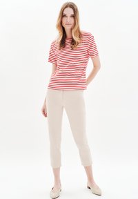 Rood-wit gestreepte T-shirt met korte mouwen, gecombineerd met lichtbeige cropped broeken. Schoeisel zijn lichtgekleurde, lage hakken.