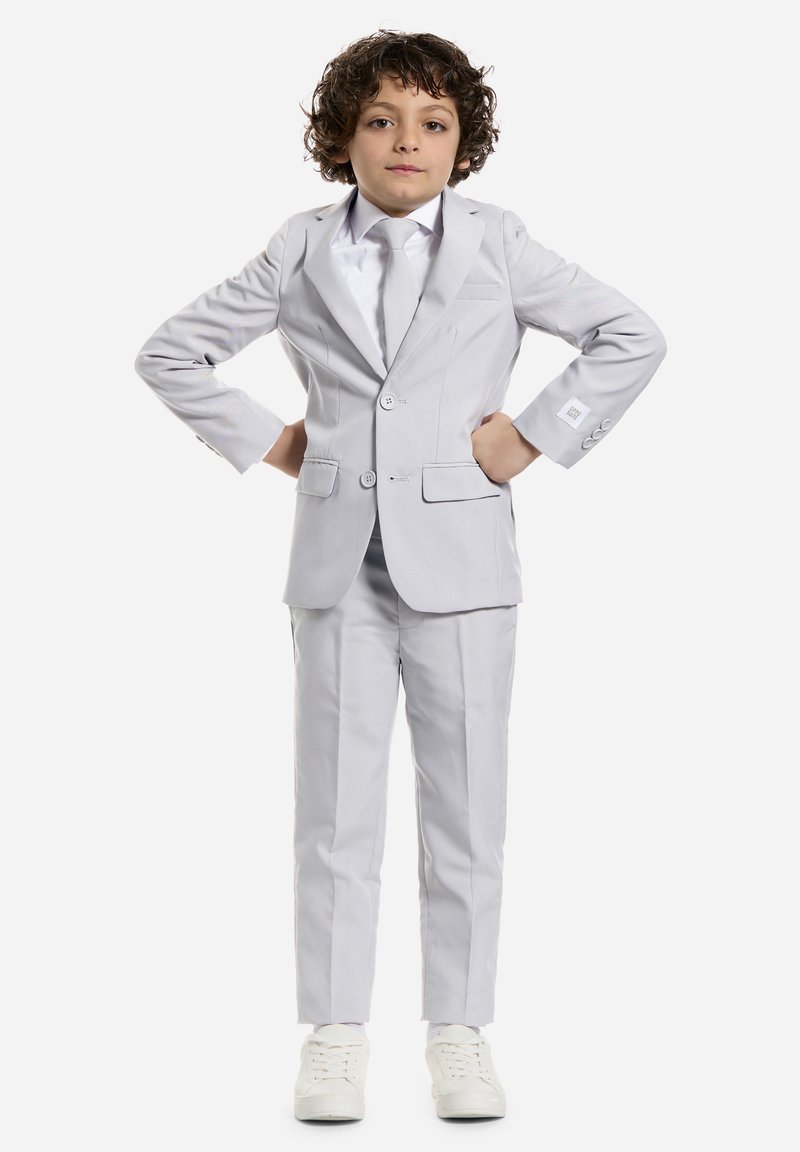Completo grigio chiaro con due bottoni, pantaloni coordinati e una camicia bianca. Indossato con sneakers bianche, caratterizzate da una texture liscia e una sartoria ordinata.