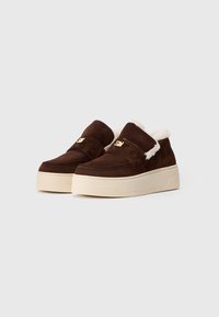 Pantofi slip-on din suede maro, cu interior din blană crem, talpă groasă din cauciuc bej și logo-ul auriu "SM" pe curele din față.