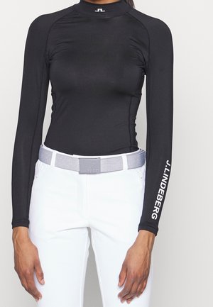 Sort, figursyet langærmet top med J.LINDEBERG-logo på ærmet, stoppet ned i hvide bukser med et lysegråt bælte og firkantet spænde.