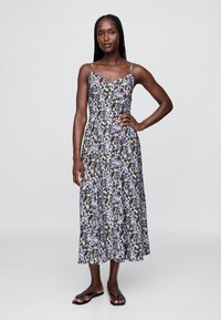 Blumiges Midikleid mit dünnen Spaghettiträgern, mit einem lila-schwarzen Muster auf weißem Hintergrund, aus leichtem Stoff gefertigt.