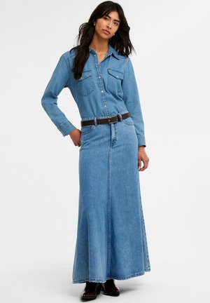 Denim maxijurk met lange mouwen, knoopsluiting, twee borstzakken en een aansluitende taille; heeft een donkerbruine leren riem en een zijsplit.