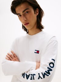 Biała longsleeve z małym logotypem na piersi oraz napisem "TOMMY JEANS" w granatowym kolorze na rękawie. Gładki materiał z bawełny.