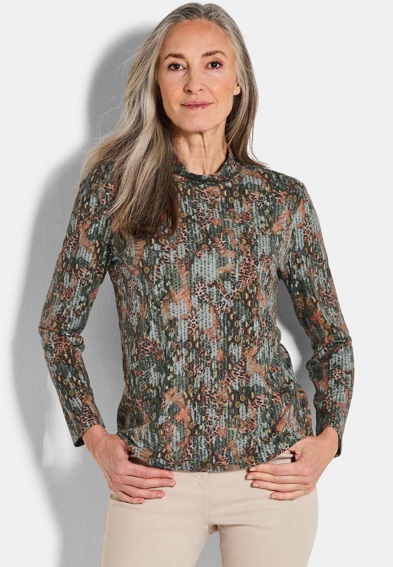 Langarmshirt in groen, bruin en oranje patronen. Heeft een ronde hals en een gestructureerde stof met verschillende ontwerpen.