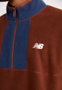 Maglia in pile mezza zip marrone e blu con texture spazzolata, colletto alto e accento logo bianco sul petto.