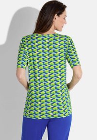 Haut à manches courtes avec un motif géométrique vert, bleu et jaune ; tissu doux ; coupe ample ; encolure ronde ; vue arrière mettant en valeur le motif et le design.