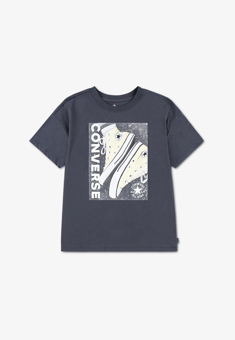 T-shirt en coton bleu marine avec un imprimé graphique de baskets Converse jaunes, texte blanc et fond gris texturé.