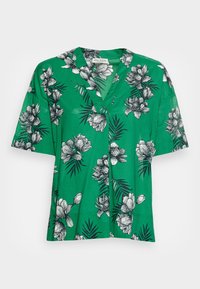 Camisa verde de manga corta con escote en V, que presenta patrones de flores y hojas negros sobre una tela ligera. Corte holgado con dobladillo recto.