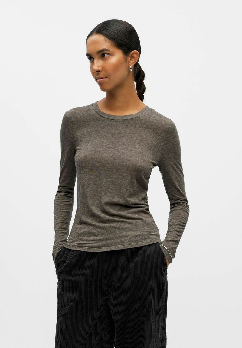 Maglietta a maniche lunghe e collo rotondo in tessuto marrone melange; design aderente con texture liscia e leggero splendore. Abbinata a pantaloni in velluto a coste neri.