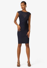 Marineblaue Bodycon-Kleid mit kurzen Ärmeln, mit strukturierten Streifen und einer taillierten Silhouette. Getragen mit schwarzem, absatzschuhen.