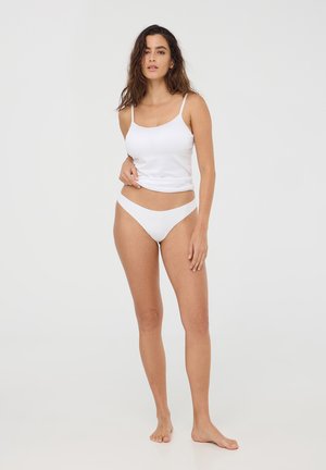 Canottiera bianca in cotone con spalline sottili abbinata a slip bikini bianchi coordinati. Texture liscia, design aderente, cuciture minime, senza motivi.