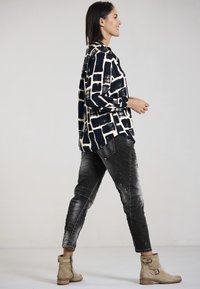 Lässiges, langärmliges Hemd in Marineblau mit einem abstrakten cremefarbenen Muster, kombiniert mit verwaschenen schwarzen Jeans und braunen Stiefeletten mit Riemen.