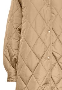 Beige kviltad jacka med diamantstickning, tryckknappar och lång ärm, visad från midjan till handleden.