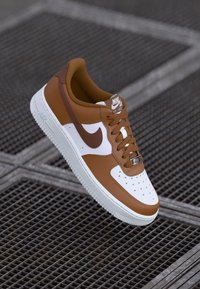 Rudas ir baltas odinis sportbačių modelis su perforuota pirštine, raišteliais priekyje ir šviesiai ruda vidumi; su išskirtiniu 'swoosh' logotipu.