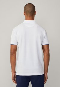 Λευκό πόλο πουκάμισο με κοντά μανίκια, διακοσμημένο με μπλε λεπτομέρειες στους μανικετόντες. Μαλακή υφή, ίσια τελειώματα και κλασικός σχέδιο κολάρου.