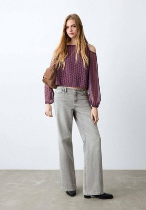 Blusa morada con estampado, de hombros descubiertos y mangas largas, combinada con vaqueros de pierna ancha gris claro y botines negros; bolso marrón al hombro.