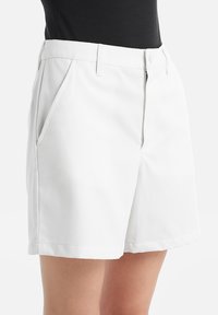 Pantaloni corti bianchi con vestibilità sartoriale, dotati di tasche laterali, una texture liscia, design plissettato e lunghezza a metà coscia.
